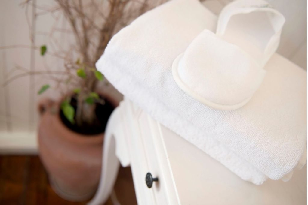 Folded white towel with spa slippers on a white nightstand beside a terracotta planter with greenery