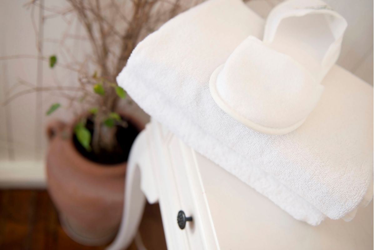 Folded white towel with spa slippers on a white nightstand beside a terracotta planter with greenery