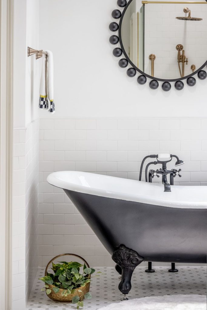 Clawfoot bathtub with black exterior, round mirror, and white tile in a remodeled bathroom in Chapel Hill, North Carolina