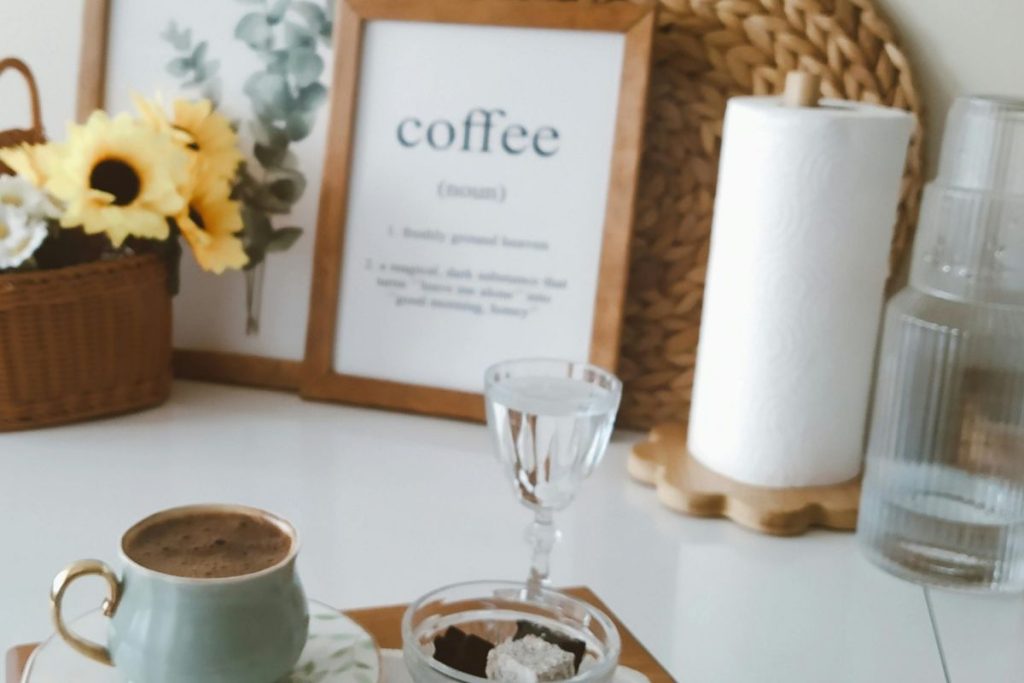 Home coffee station with cup of coffee, glass of water, chocolate treats, and framed coffee quote on a white countertop
