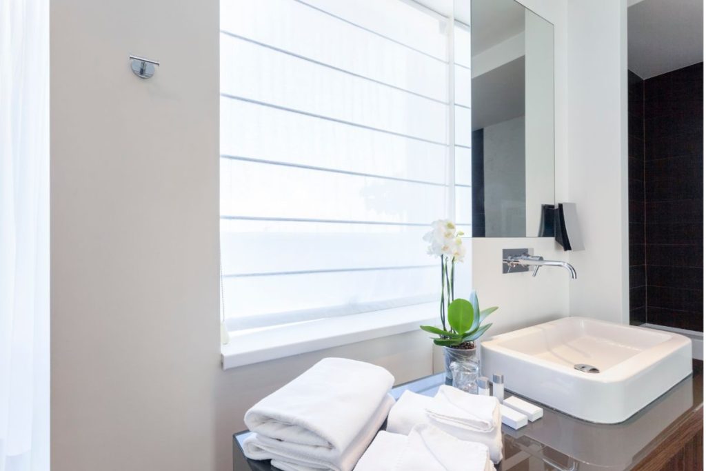 Minimalist bathroom counter with white towels, an orchid plant, and a modern sink beneath a large mirror