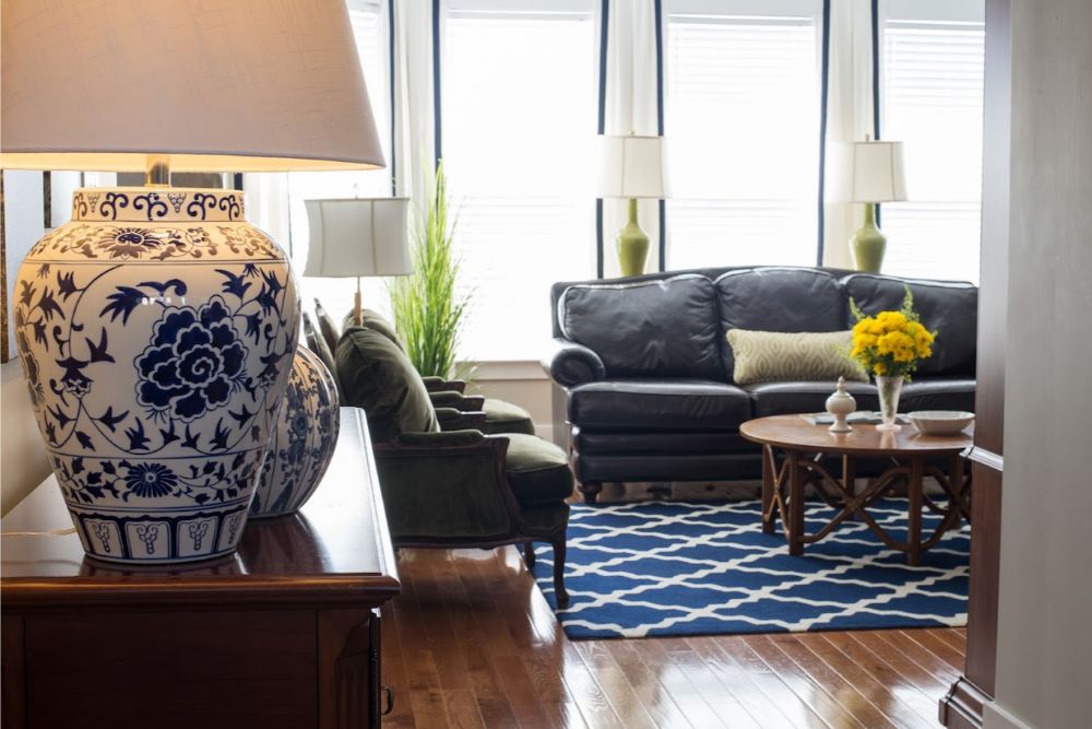 Durham living room with green velvet armchairs, dark leather sofa, and blue-and-white ceramic lamp on wood floors
