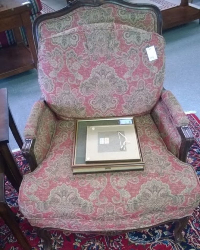 Antique armchair with red and beige damask fabric, shown before reupholstery in a showroom setting
